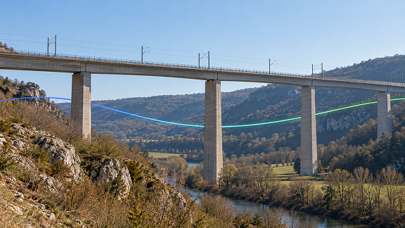 Railway viaduct crossing a rural valley, with a digital light trail illustrating long-distance optical network connectivity.